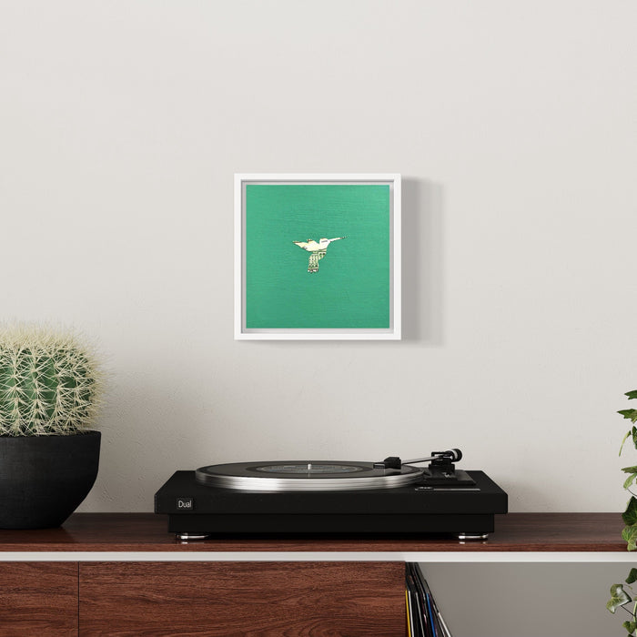 The artwork 'Profit Margins, Hummingbird' by Jacki Davis features a delicate white hummingbird silhouette crafted from US currency against a vibrant emerald green background. The minimalist composition, set in a white frame, showcases the intricate details of the collaged currency on an 8x8 inch wood panel with acrylic medium.